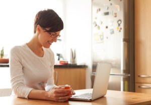Beautiful young woman with coffee using laptop in the kitchen
